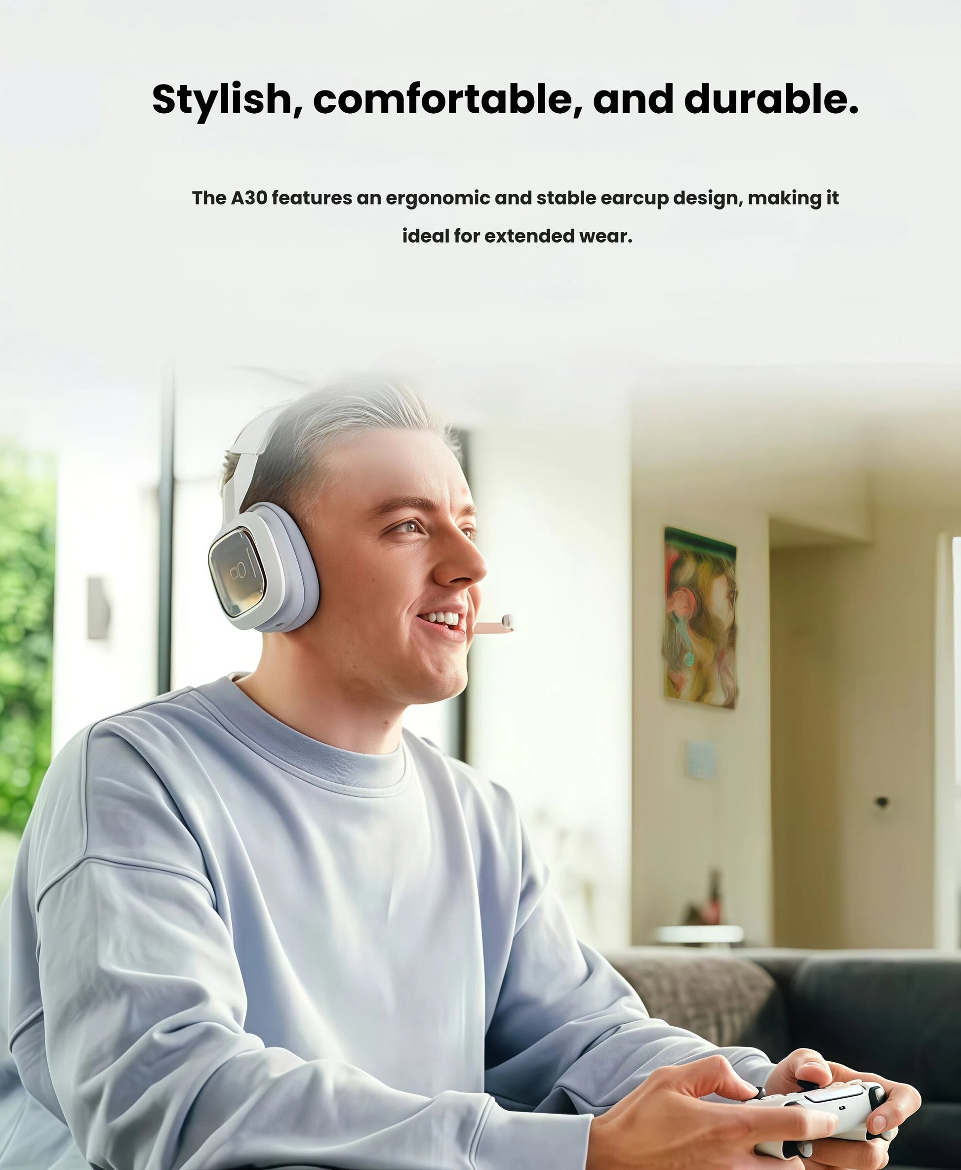 Lifestyle shot of a smiling player in a modern living room wearing the white ASTRO A30 while holding a controller, illustrating extended-wear comfort.