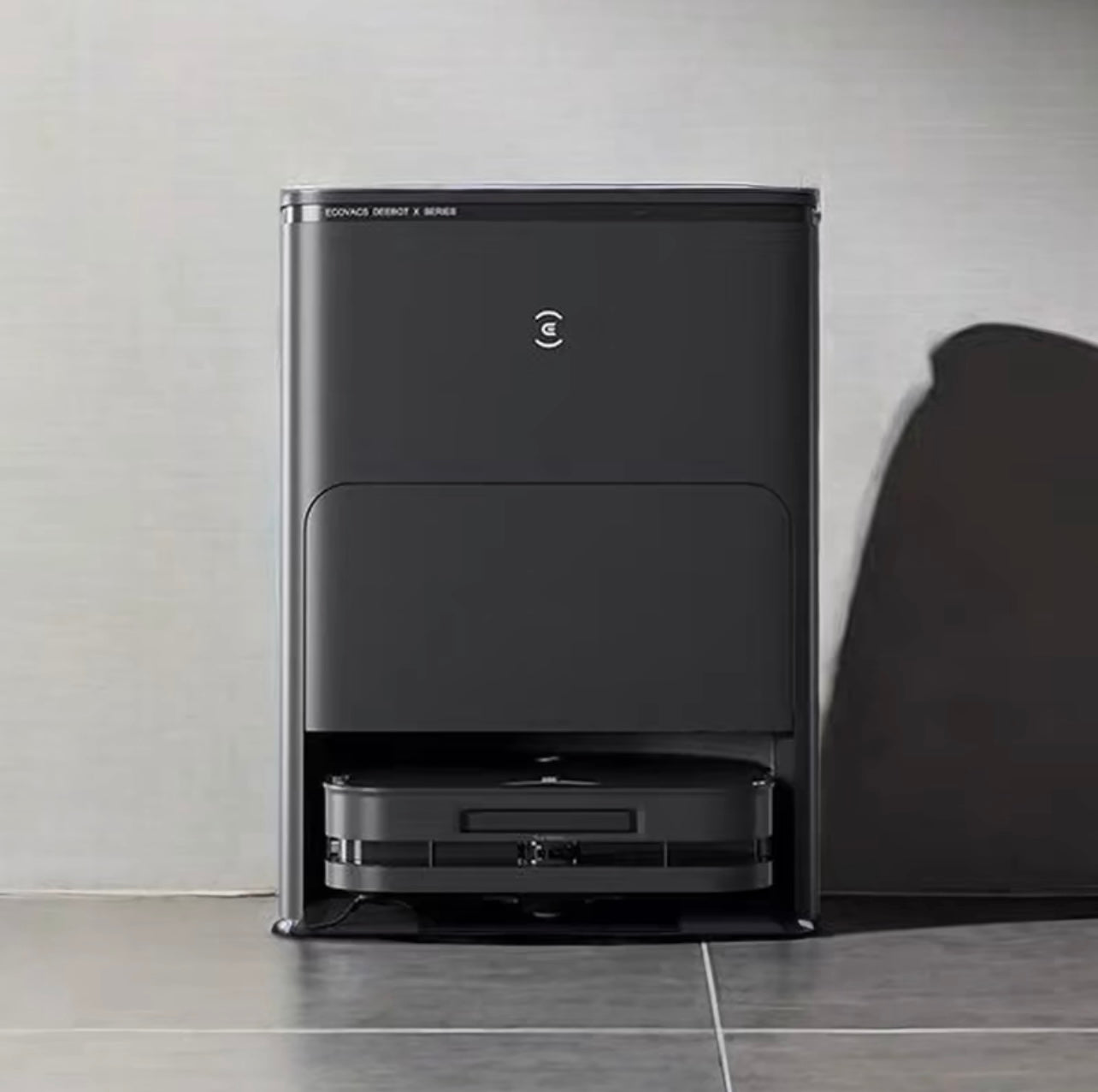 Image of the Ecovacs X5 Pro Omni, a sleek, black robot vacuum cleaner with its charging and cleaning base. The robot is docked in the station, featuring a modern design with a glowing blue indicator light on the front of the robot. The station has a minimalist look, designed for automatic cleaning and maintenance of the robot
