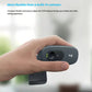 Hand holding the small Logitech C270 webcam, demonstrating its portable, adjustable design for laptops, monitors, or tripods.