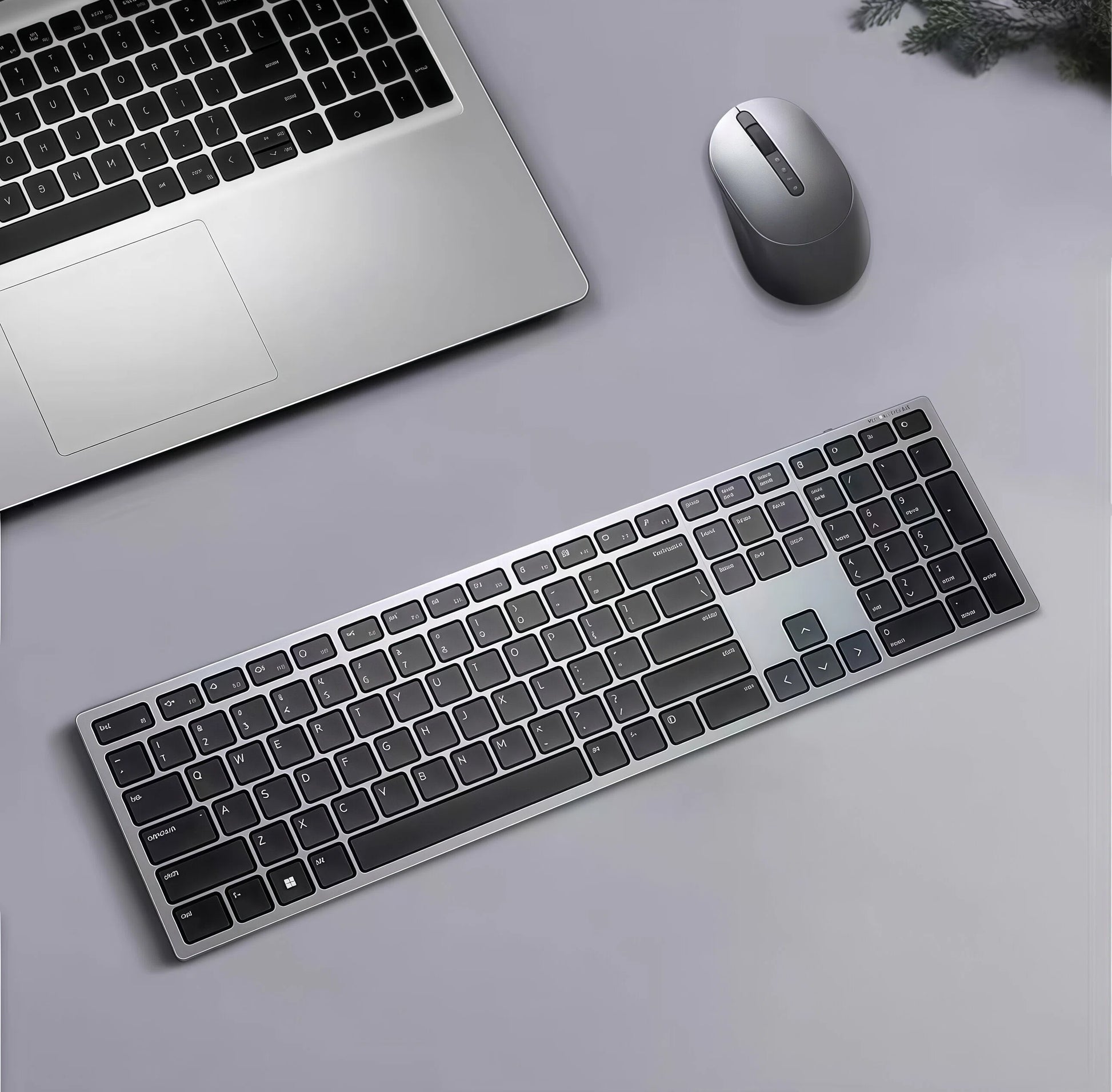 Top-down view of the Dell KM7321W wireless keyboard and mouse placed next to a silver laptop on a gray desk. The sleek design complements modern workspaces, offering seamless wireless connectivity and quiet operation for daily computing tasks.