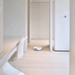 A white Ecovacs T30 Pro Omni robot vacuum cleaner operating in a modern kitchen with light-colored hardwood floors. The kitchen features sleek, minimalistic cabinetry and a built-in black and silver Toshiba oven