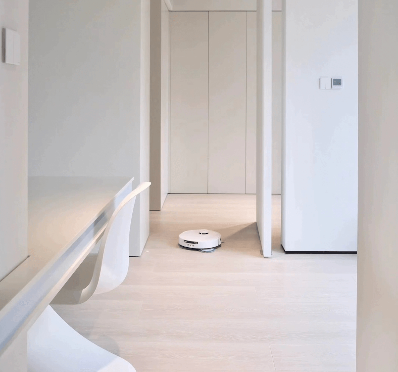 A white Ecovacs T30 Pro Omni robot vacuum cleaner operating in a modern kitchen with light-colored hardwood floors. The kitchen features sleek, minimalistic cabinetry and a built-in black and silver Toshiba oven