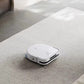 A white Ecovacs Deebot X2 Omni robot vacuum cleaner operating on a light-colored rug in a modern living room. The vacuum is seen cleaning efficiently, with a portion of the sofa and floor visible in the background.