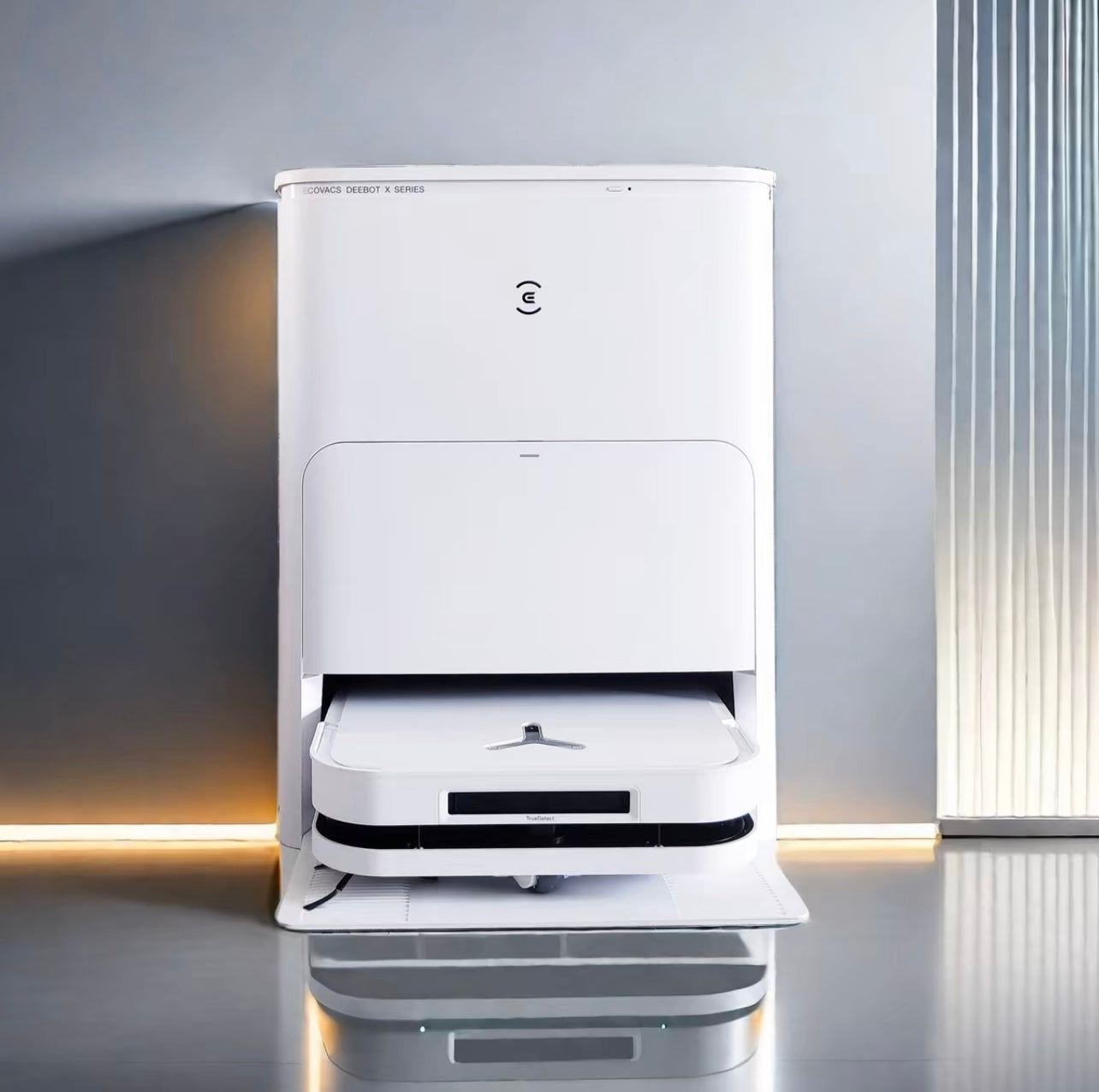 Image of the Ecovacs X5 Pro Omni, a sleek, white robot vacuum cleaner with its charging and cleaning base. The robot is docked in the station, featuring a modern design with a glowing blue indicator light on the front of the robot. The station has a minimalist look, designed for automatic cleaning and maintenance of the robot