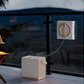 The ECOVACS Winbot W2 Pro robotic window cleaner is shown cleaning a glass balcony railing at dusk, with its portable base station resting on the wooden deck, providing a clear and sparkling view.