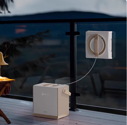 The ECOVACS Winbot W2 Pro robotic window cleaner is shown cleaning a glass balcony railing at dusk, with its portable base station resting on the wooden deck, providing a clear and sparkling view.