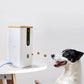 Black-and-white dog catching treats launched by the DOGNESS 8065 Wi-Fi camera on a white table, showcasing remote treat tossing.
