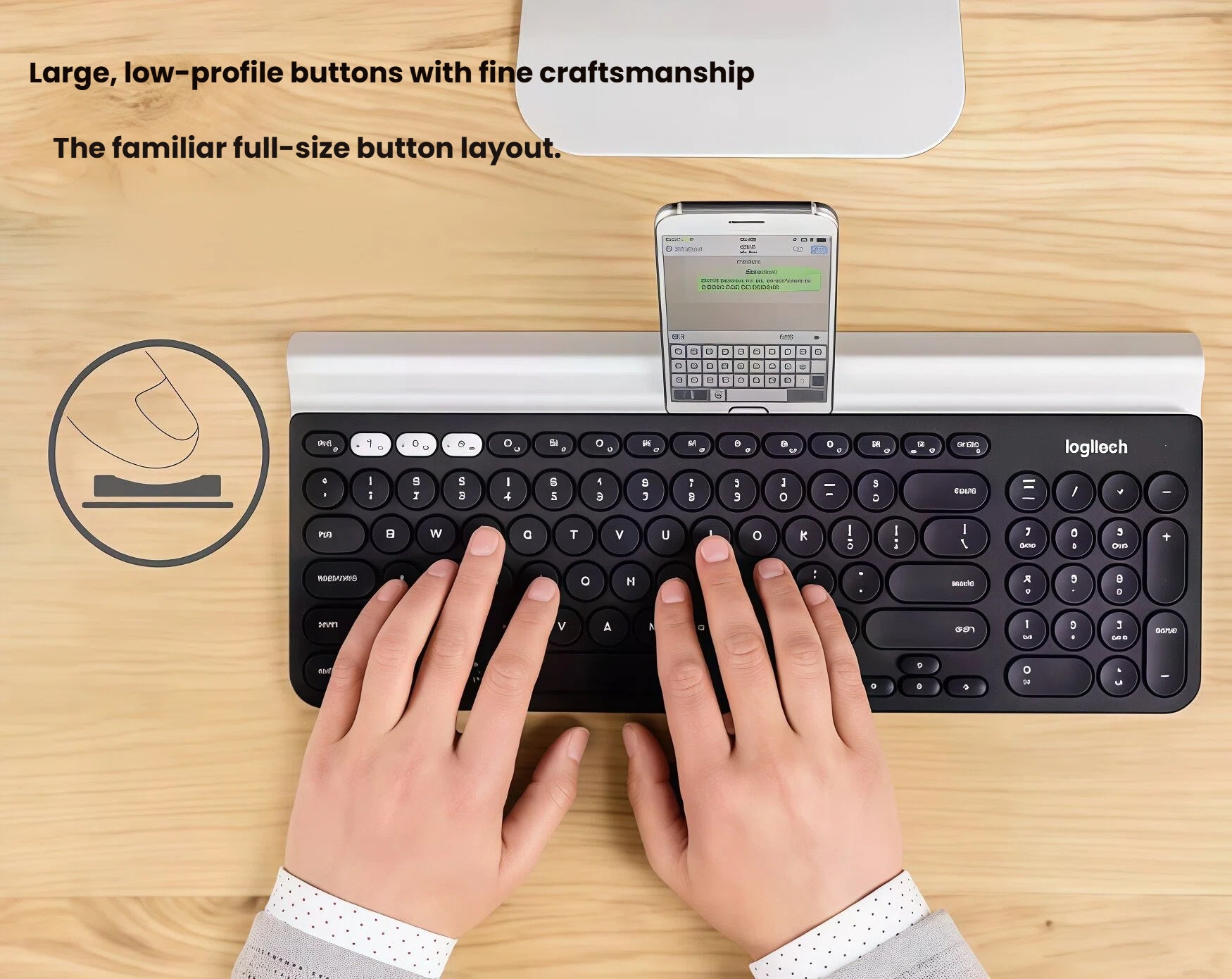Hands typing on the Logitech K780 while a smartphone rests in the keyboard’s rubber cradle, emphasizing large low-profile keys and ergonomic layout for everyday productivity.