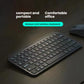 Lifestyle photo of the graphite Logitech MX Keys Mini illuminated wireless keyboard on a dark wood desk next to a Logitech mouse, emphasizing compact portability and comfortable office use.