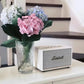  Bright lifestyle shot of the cream Marshall Stanmore III speaker placed next to a vase of pink and blue hydrangeas on a white console table, ideal for home styling inspiration.
