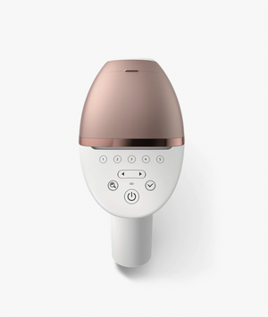 Image of a handheld IPL (Intense Pulsed Light) hair removal device in a sleek white and rose gold design. The device comes with three interchangeable attachment heads for different body areas, each designed with specialized treatment windows. The attachments are color-coded for easy identification and suited for face, body, and precision areas