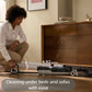 A woman easily cleaning under a low-profile dresser with the Roborock F25 ACE in its lay-flat position, which has a clearance height of just 4.92 inches for getting under beds and sofas.