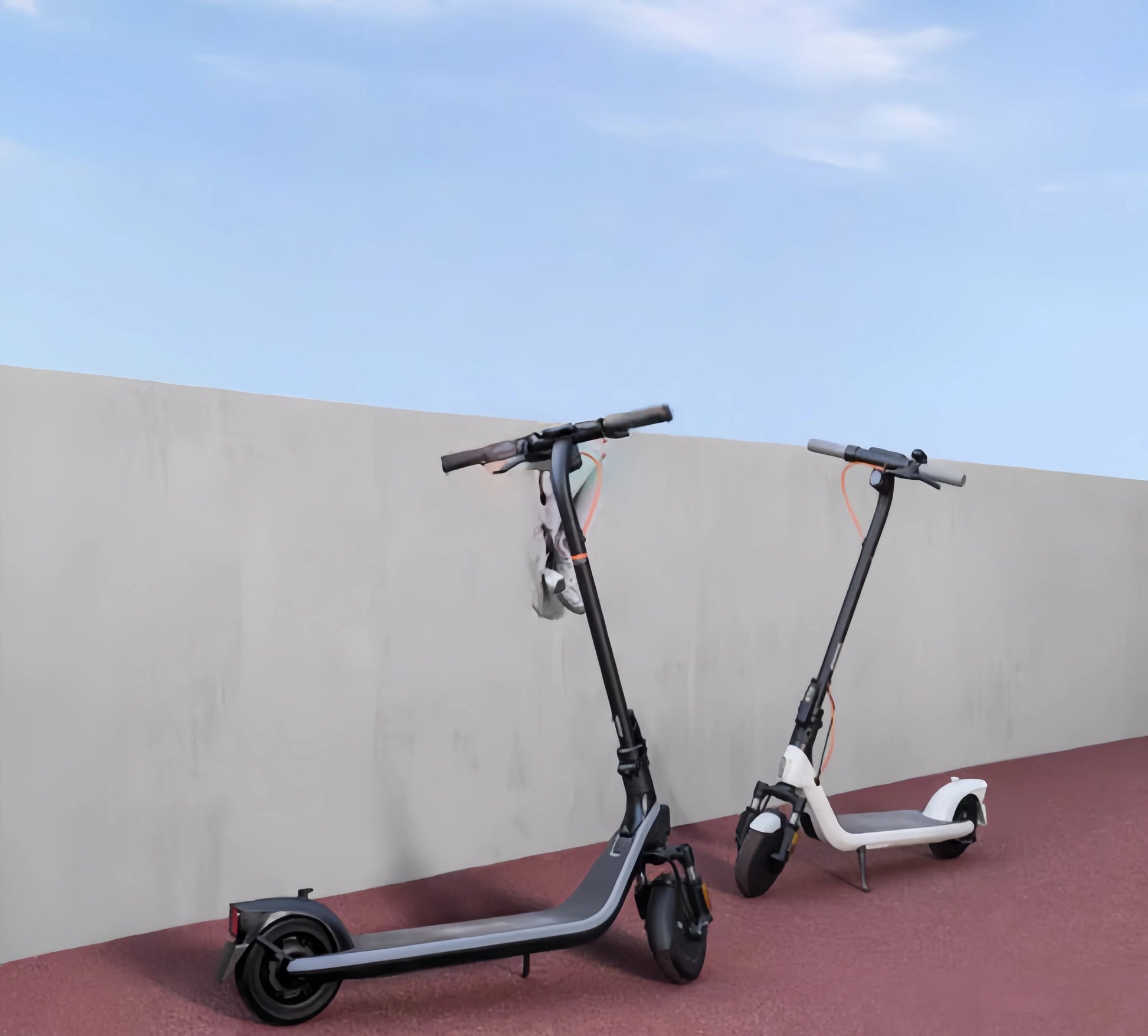 The Segway E2 Plus electric KickScooter shown in both black and white color options, parked side-by-side on a colored path.