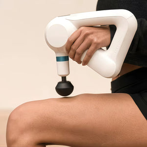 Close-up of white Theragun Elite G5 gliding over thigh, demonstrating deep-tissue percussion therapy for muscle recovery.