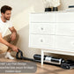 A man uses the Tineco FLOOR ONE S7 Stretch SteamFree's 180° lay-flat design to easily clean hidden dust under a low white dresser, showing its ability to reach difficult areas.