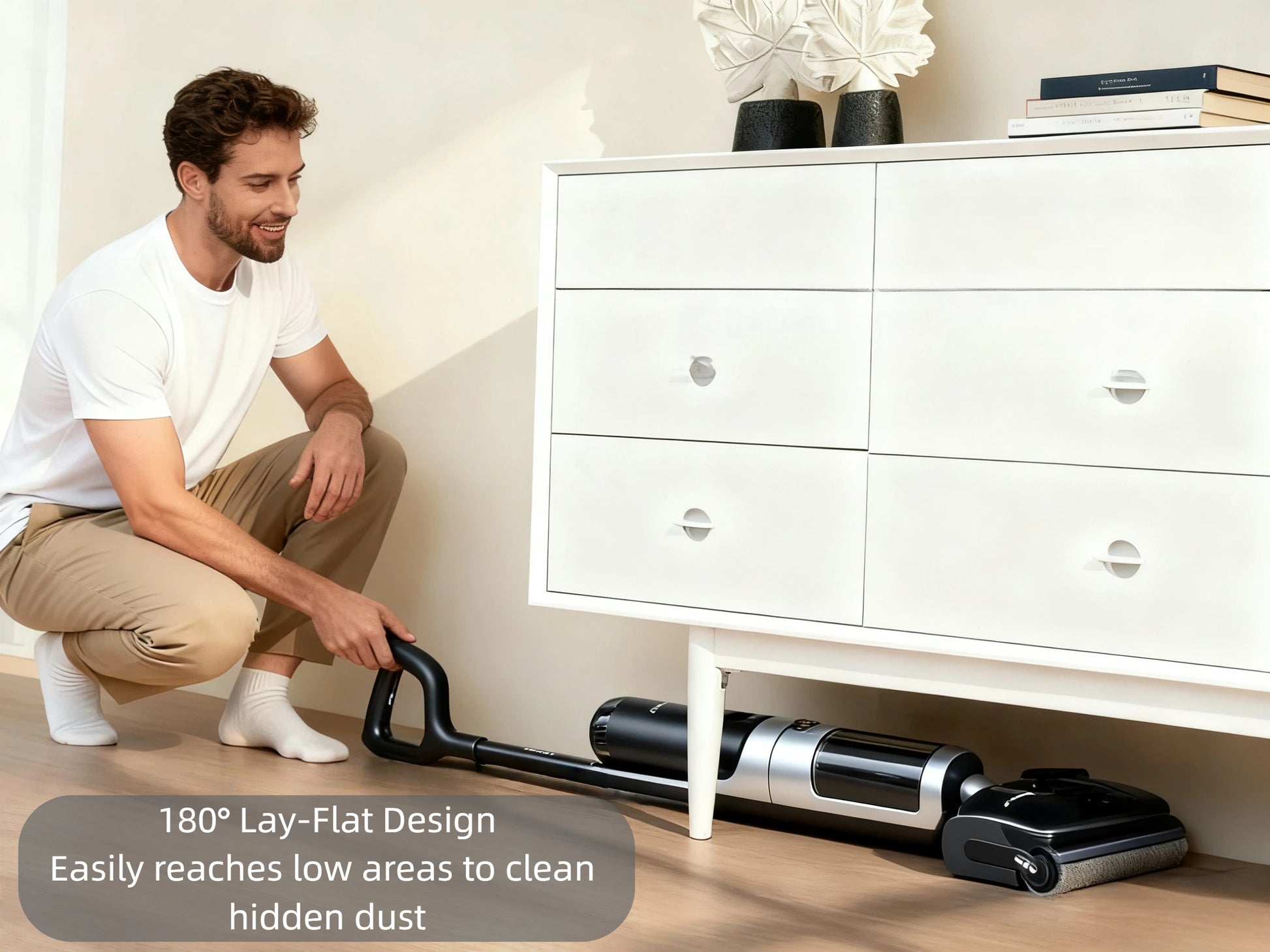 A man uses the Tineco FLOOR ONE S7 Stretch SteamFree's 180° lay-flat design to easily clean hidden dust under a low white dresser, showing its ability to reach difficult areas.