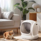 Orange tabby cat sitting beside UB Pet by Pettecc C20 self-cleaning litter box in a modern living room with sofa and plants, showcasing pet-friendly design and home integration