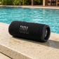 JBL Flip 6 waterproof black speaker resting on a ledge beside a pool