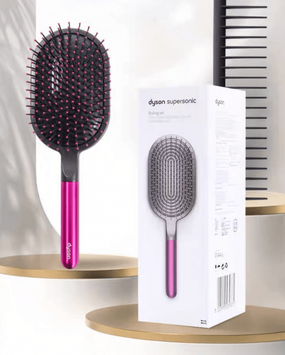 Image of a hair care set featuring a wide paddle brush with a curved design and pink handle, alongside a black wide-tooth comb. The brush has a flexible, ventilated structure with rounded bristles for gentle detangling, while the comb, labeled with the 'Dyson' logo, is designed for precise styling and easy detangling of wet or dry hair.