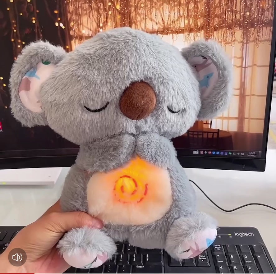 Video of the breathing koala plushie, soft and grey colour with a pink light in the tummy area. Makes relaxing sounds that soothe anxiety and appears to be fluffy and soft. Also makes breathing motion and there is a yellow light n the centre with music 